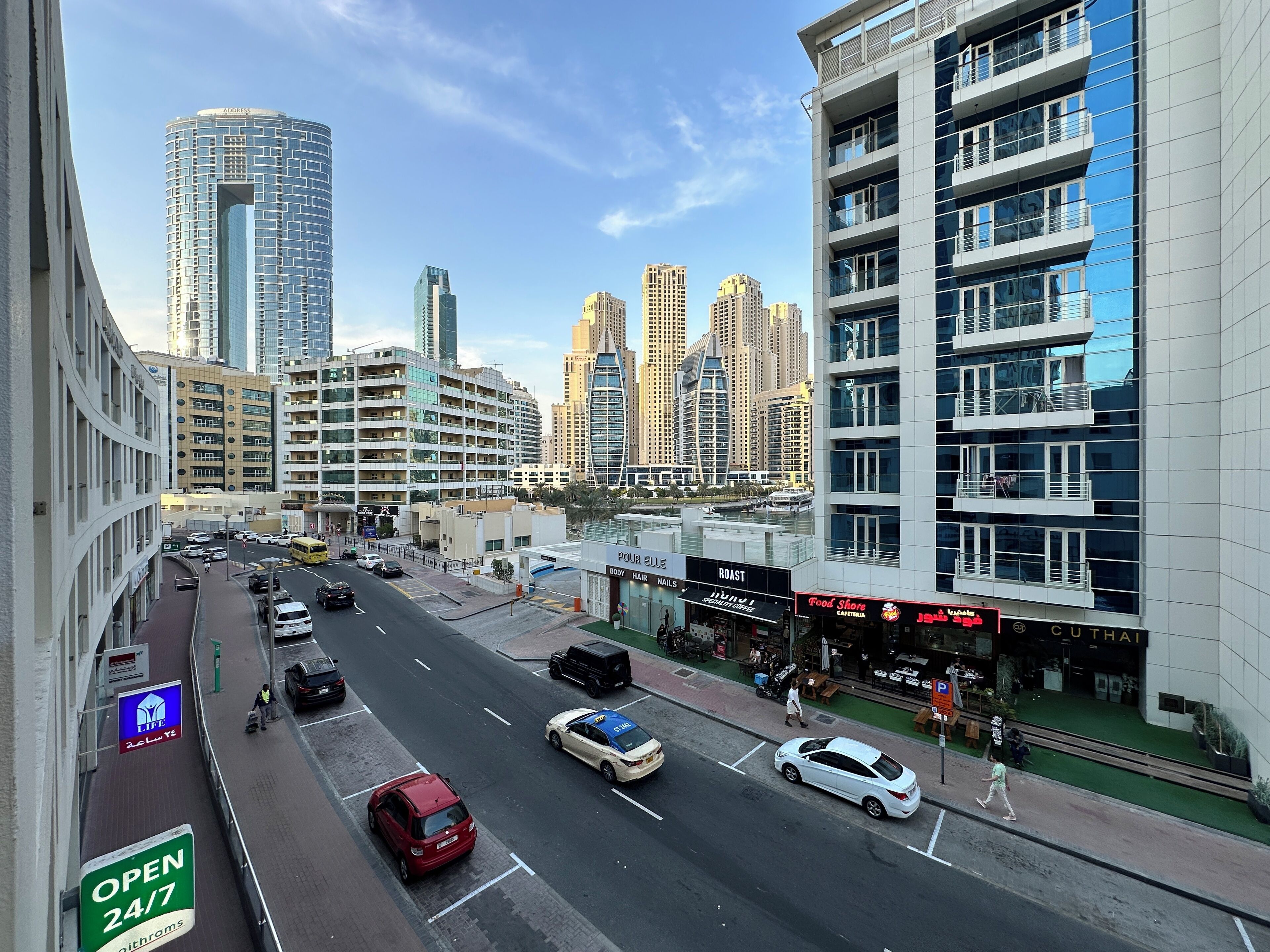 A city street with modern buildings, a variety of shops, and a clear sky.