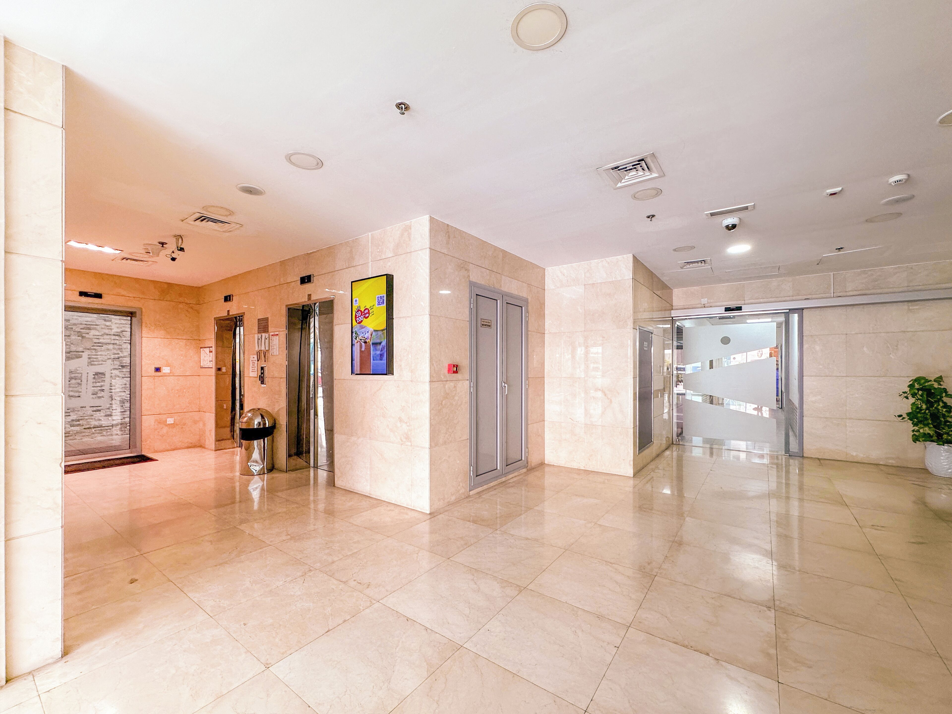 A spacious lobby with a marble floor, multiple elevators, and a potted plant.