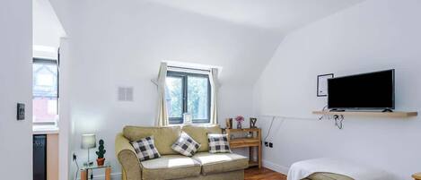 A living room with a sofa, a TV, a window, and a small table.
