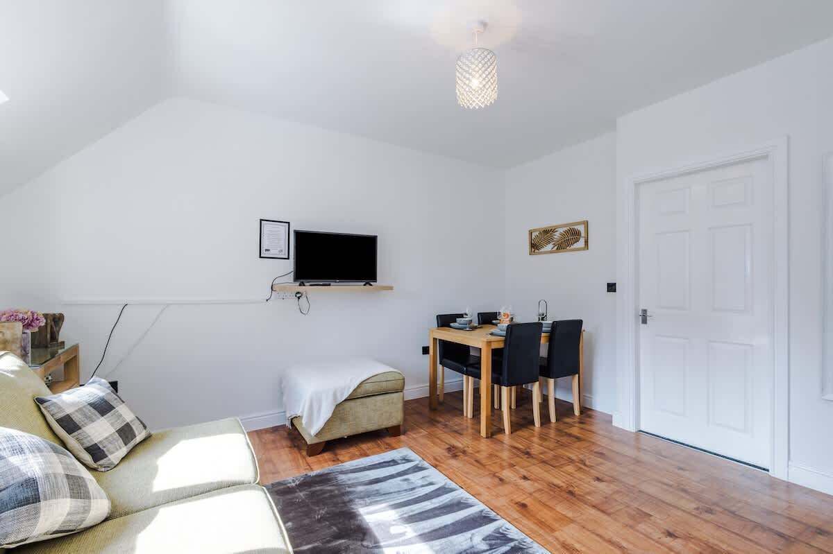 A room with a sofa, a dining table with chairs, a television mounted on the wall, and a door.