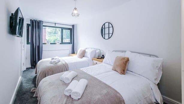 Une chambre d’hôtel avec deux lits, une télévision, une fenêtre avec des rideaux, un luminaire suspendu et un miroir fixé au mur.