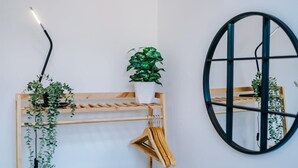 Une pièce avec un portant en bois où sont suspendus des vêtements, une plante en pot et un miroir rond accroché au mur.