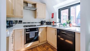Une cuisine moderne avec des meubles en bois clair, un lave-vaisselle noir et une fenêtre donnant sur des immeubles.