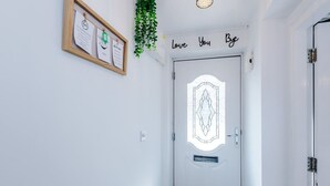 Une porte blanche ornée d’un panneau de verre décoratif, une pancarte avec l’inscription « Je t’aime, au revoir » au-dessus, et un tableau d’affichage encadré accroché au mur.