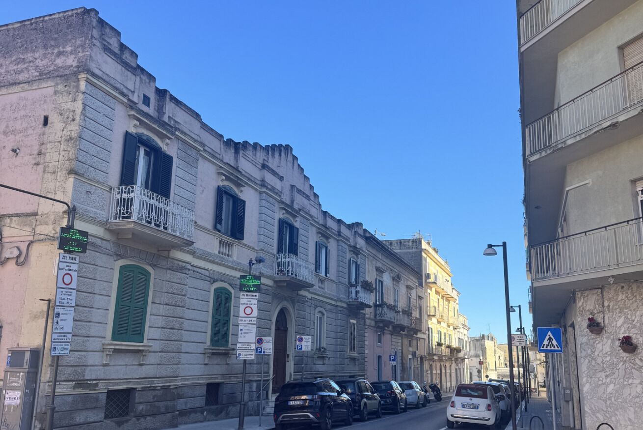 A narrow street lined with historic buildings, some with balconies and signage indicating parking restrictions.