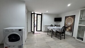 A laundry room with a washing machine, a dining area with a table and chairs, and a television mounted on the wall. - Holiday Properties nei Sassi Home (Matera)