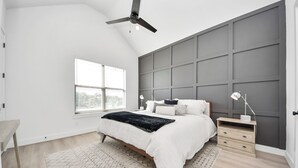 Ein modernes Schlafzimmer mit einem Bett, Nachttischen, einem Deckenventilator und einem großen Fenster.