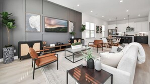 Ein modernes Wohnzimmer mit Sofa, Couchtisch und Fernseher. Im Hintergrund befindet sich ein Essbereich mit Stühlen und eine Küche.