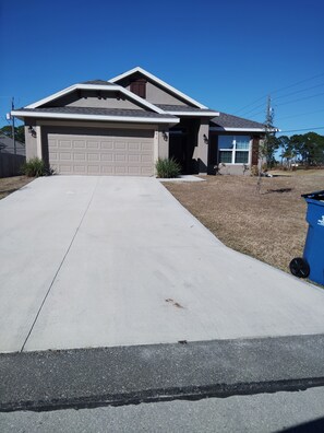 A residential house with a garage, driveway, and a blue trash bin. - Spacious 4-bedroom house in superb Palm Bay with AC (Palm Bay)