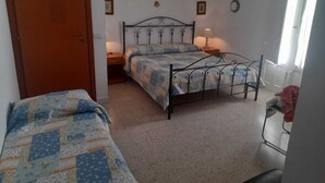 Ein Schlafzimmer mit zwei Betten, einer Holztür, einem kleinen Nachttisch mit Lampe und einer Wanduhr.