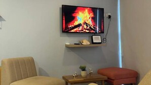 A living room with a television mounted on the wall displaying a fireplace image, a ceiling fan, and two chairs. - Hermoso alojamiento centro (Cartagena)