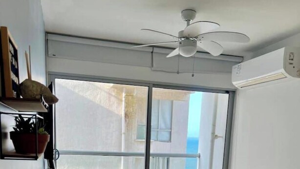 A modern living room with a sofa, a chair, a small table, and a ceiling fan. There is a large window providing a view of the outside. - Hermoso alojamiento centro (Cartagena)