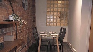 A dining area with a brick wall, a window with a grid pattern, and a table set for four. - Cosy 3-Bedroom Family Apartment - Free Parking (Birmingham)