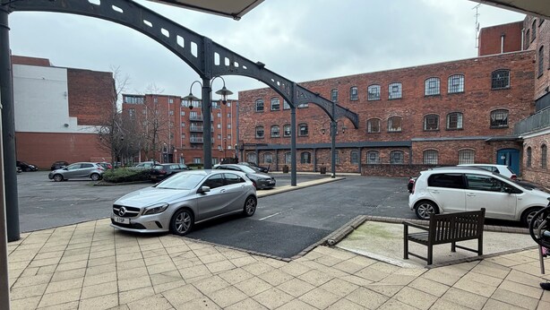 A parking area with cars, a bench, and a building with brick walls and multiple windows. - Cosy 3-Bedroom Family Apartment - Free Parking (Birmingham)