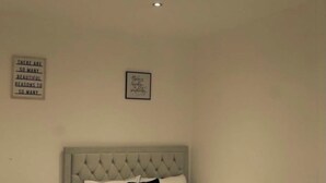 A bedroom with a tufted headboard bed, a bedside table with a lamp, and two wall-mounted signs. - Cosy 3-Bedroom Family Apartment - Free Parking (Birmingham)