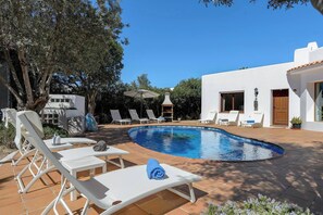 A swimming pool with lounge chairs and umbrellas, surrounded by a white building and trees. - Live the Ibiza Experience (Sant Josep de sa Talaia)