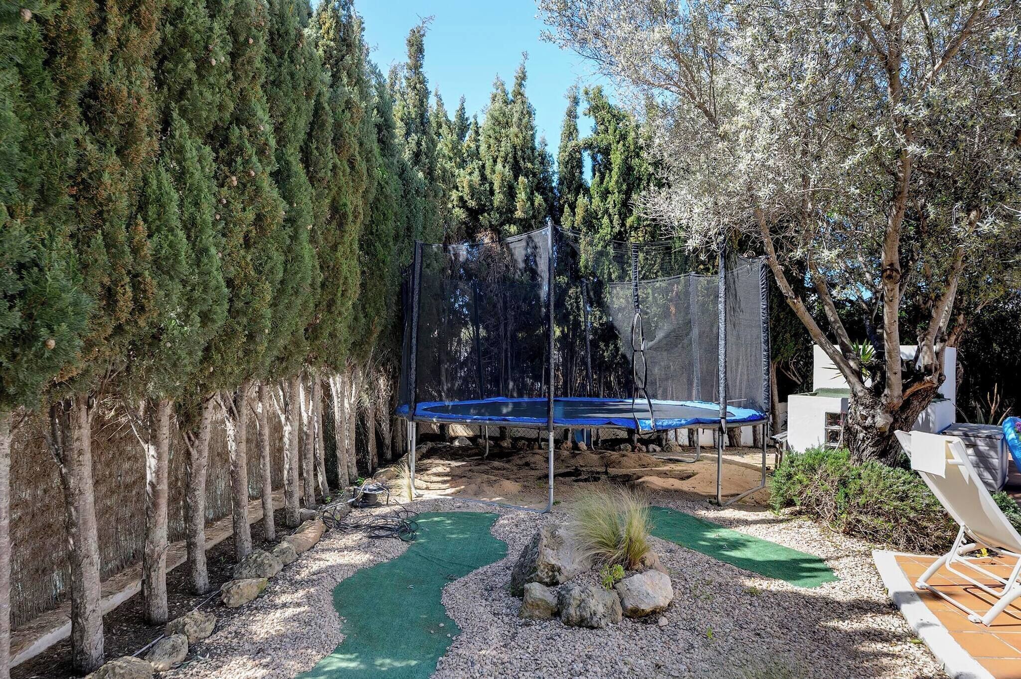 Un patio trasero con un trampolín, un pequeño estanque y una zona de estar con una silla y una mesa.