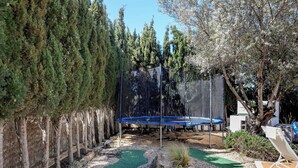 A backyard with a trampoline, a small pond, and a seating area with a chair and table. - Live the Ibiza Experience (Sant Josep de sa Talaia)
