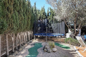 Ein Garten mit Trampolin, einem kleinen Teich und einer Sitzgruppe bestehend aus Stuhl und Tisch.