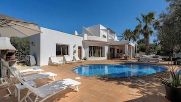 Una casa moderna con piscina, zona de estar exterior y barbacoa.