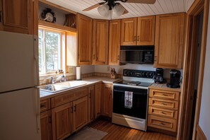 A kitchen with wooden cabinets, a refrigerator, a stove, a microwave, and a window.