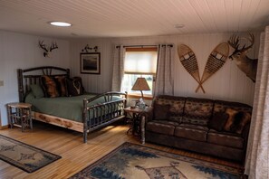 A rustic room with a wooden bed, a brown sofa, a wooden table, and two wall-mounted deer antlers.