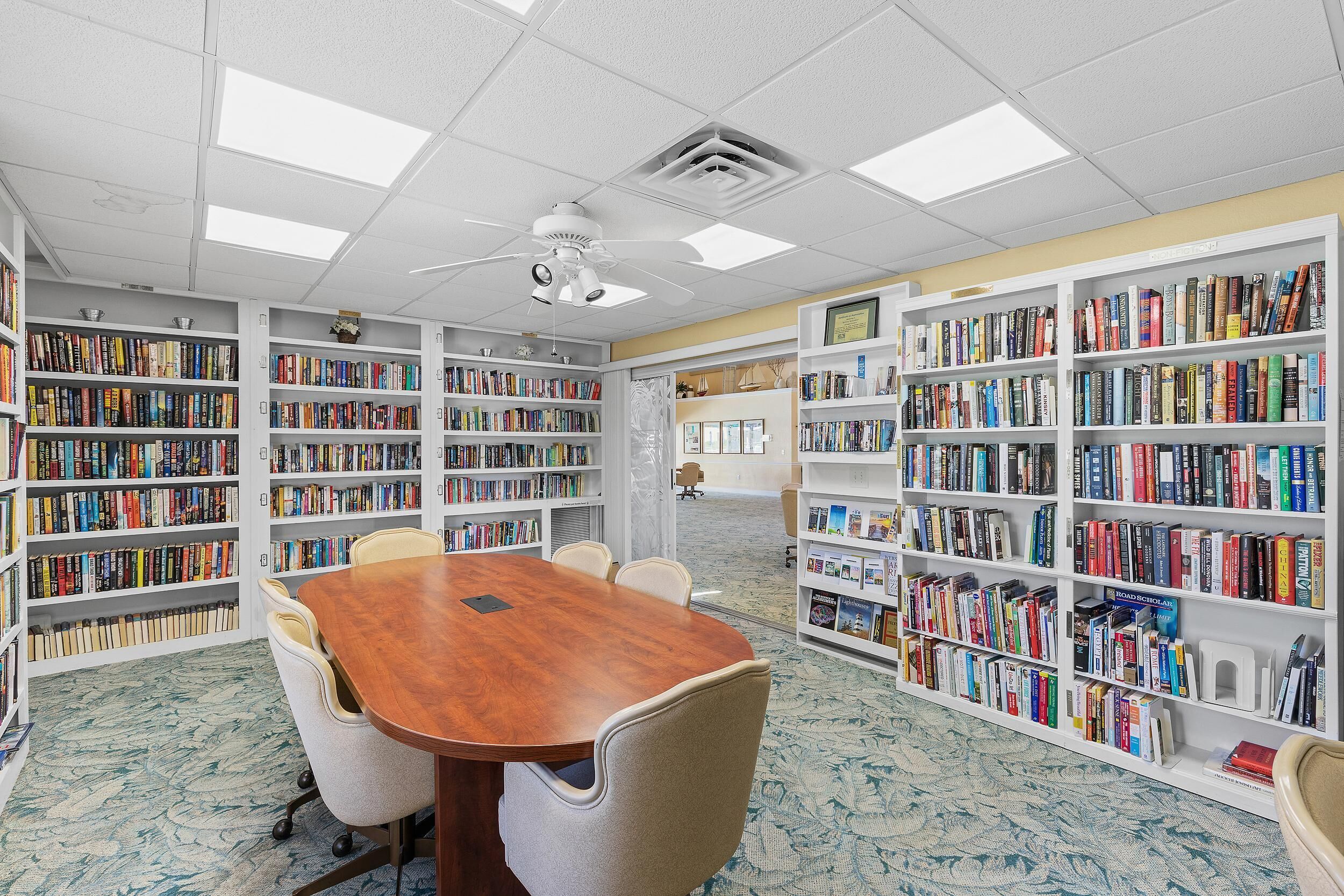 Eine Bibliothek mit einem großen Holztisch und Stühlen, umgeben von hohen Bücherregalen voller Bücher.