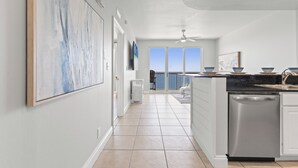 Una cocina moderna con armarios blancos, lavavajillas y vistas al océano a través de amplios ventanales.