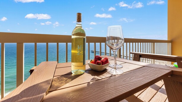 Una mesa de madera con una botella, un vaso, un cuenco de fresas y vista al océano.