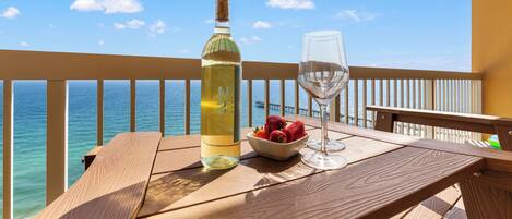 A wooden table with a bottle and a glass, a bowl of strawberries, and a view of the ocean.