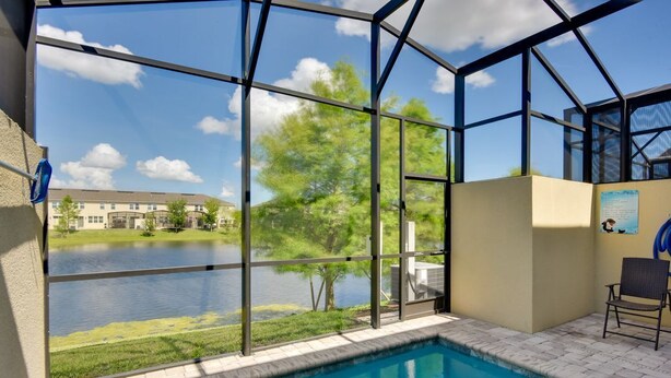 Una piscina con cerramiento de vidrio, una silla y vistas a un lago y edificios.