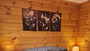 Una habitación con paneles de madera, una cama, dos lámparas de noche y tres cuadros con motivos florales en la pared.