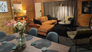Una sala de estar acogedora con interior de madera, un sofá, una mesa de centro y una mesa de comedor con manteles individuales.