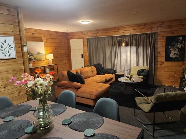 Un salon chaleureux avec un décor intérieur en bois, un canapé, une table basse et une table à manger agrémentée de sets de table.