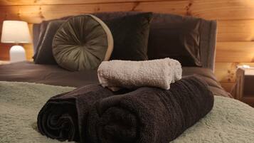 Un lit bien fait, avec une couverture verte et des serviettes enroulées, un oreiller marron foncé et un petit oreiller vert décoratif posé sur une tête de lit en bois.