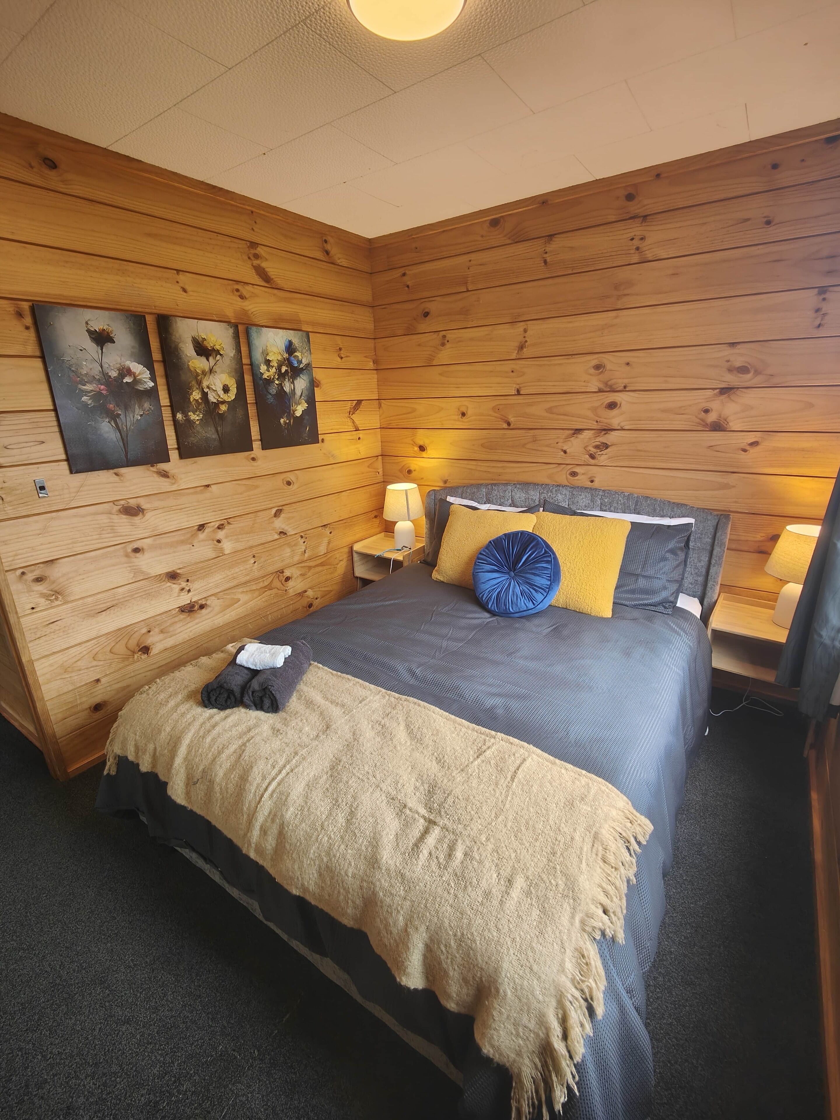 A wooden-paneled bedroom with a bed, nightstands, and wall art.