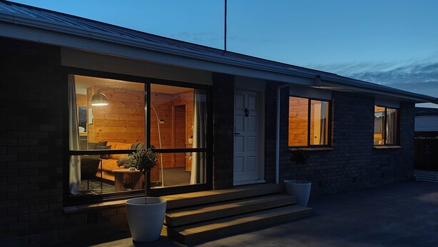 Una casa moderna con amplios ventanales, interior de madera y camino de hormigón.