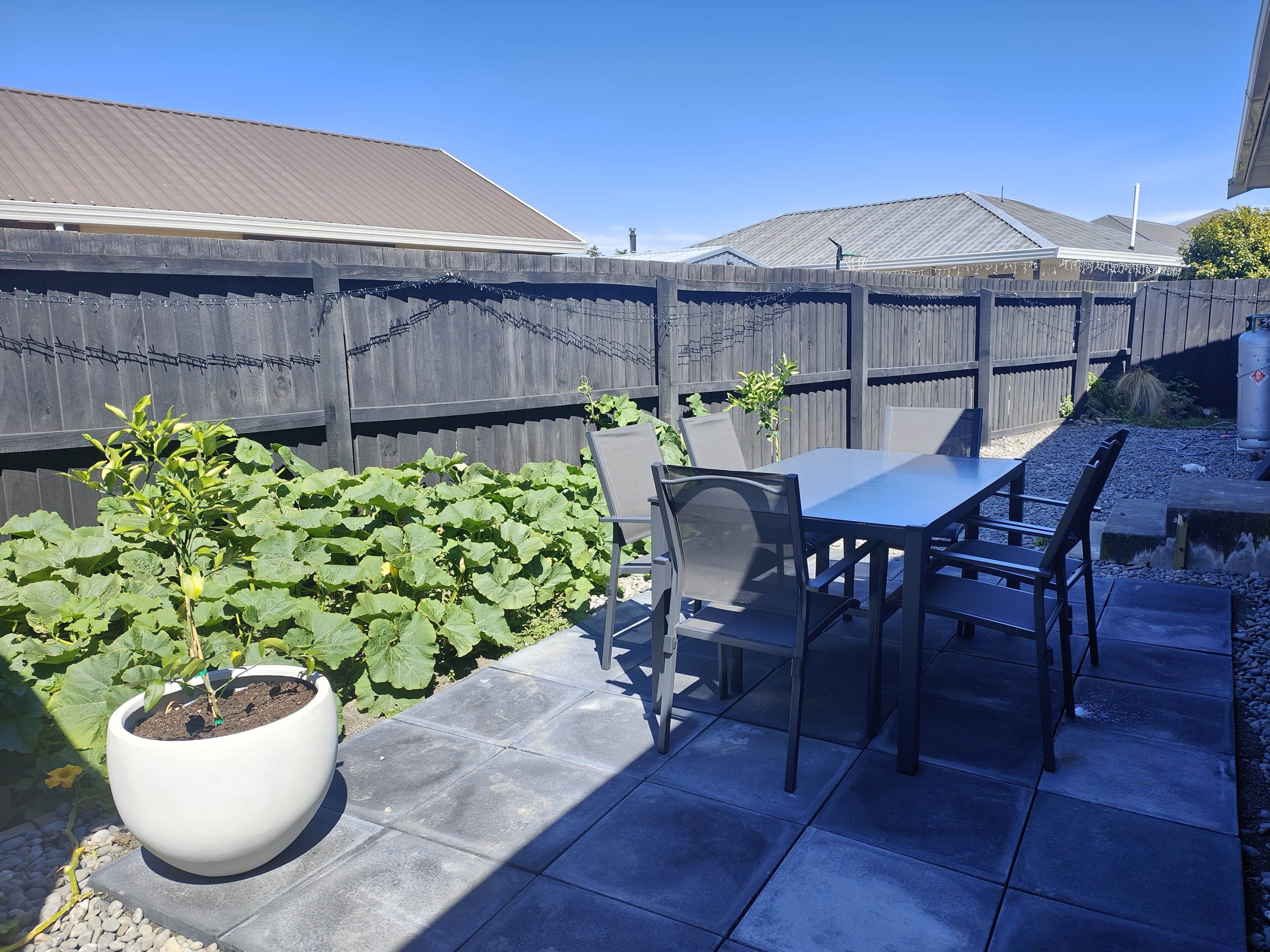 Une terrasse avec une table et des chaises, un pot de fleurs et une clôture en bois.