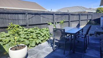 Une terrasse avec une table et des chaises, un pot de fleurs et une clôture en bois.