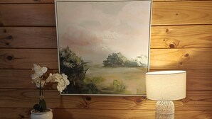 Una pared de madera con un cuadro enmarcado, una mesa blanca con una lámpara y plantas en macetas.