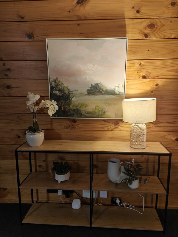 Eine Holzwand mit einem gerahmten Gemälde, ein weißer Tisch mit einer Lampe und Blumentöpfen.