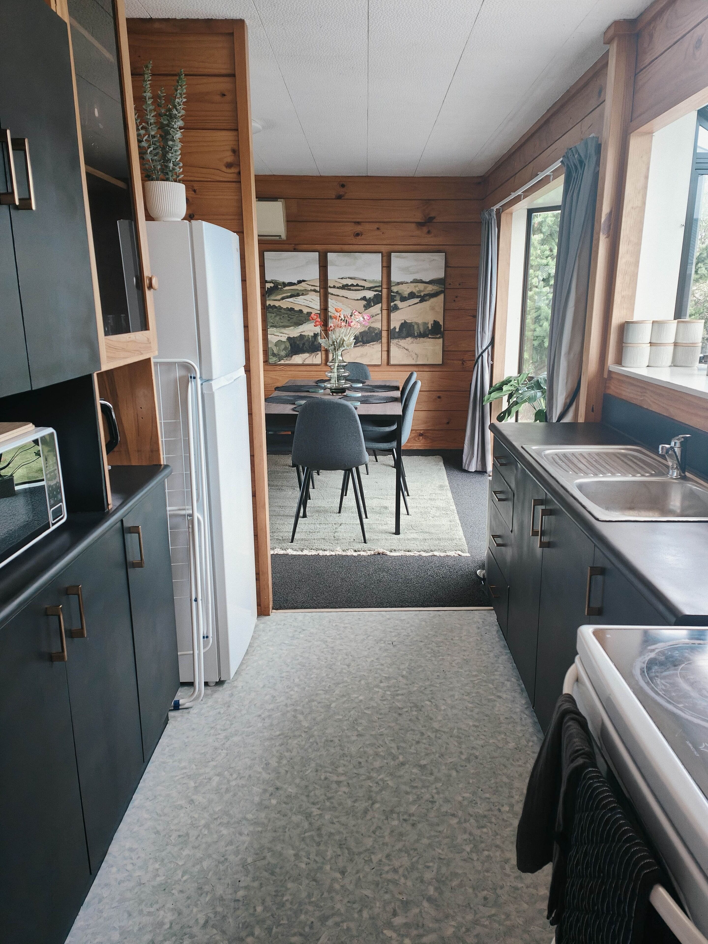Eine moderne Küche mit dunklen Schränken, einem Essbereich mit Tisch und Stühlen sowie Blick ins Freie durch große Fenster.