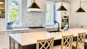 Een moderne keuken met een groot eiland, hanglampen en uitzicht op groen buiten.