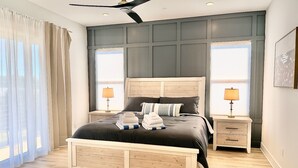 Een moderne slaapkamer met een houten bed, twee nachtkastjes met lampen, een groot raam met zonwering en een plafondventilator.