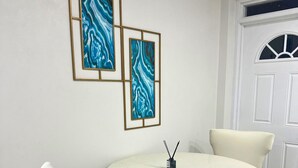 A dining area with a round table, two white chairs, and three framed abstract paintings on the wall. - Cozy 1-bedroom apartment in lovely Castries with AC (Castries)