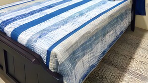 A neatly made bed with a striped bedspread, a bedside lamp, and a wall-mounted air conditioner. - Cozy 1-bedroom apartment in lovely Castries with AC (Castries)