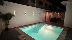 Une piscine rectangulaire dont le bord est recouvert de carreaux, entourée d’un petit muret blanc.