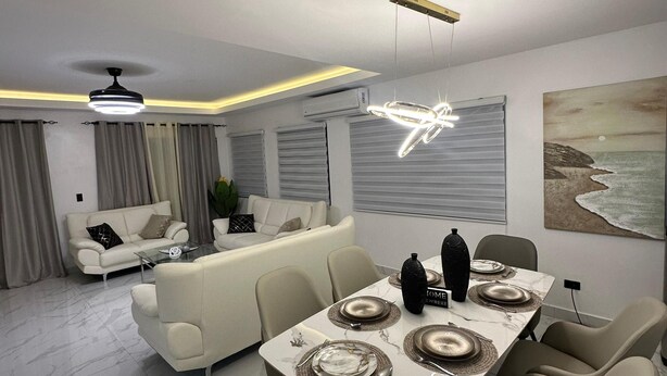 Un salon moderne avec un coin repas, doté d’un sol en marbre, de meubles contemporains et d’un grand tableau représentant une scène de plage.