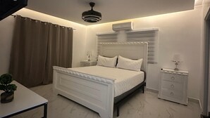 Une chambre à coucher moderne, avec un lit, des tables de chevet, une petite table, un ventilateur de plafond et une plante en pot.