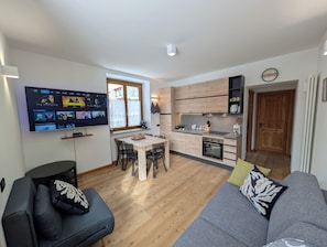 A modern kitchen with wooden cabinets, a dining table, and a TV mounted on the wall displaying a movie. - Ai piedi del Gigante apartment Cervinia-Valtournenche (Maen)